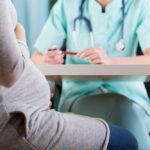 Pregnant women pictured sitting, talking to nurse.