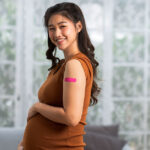 A pregnant woman smiles after receiving a vaccination, with a band aid on her upper left arm