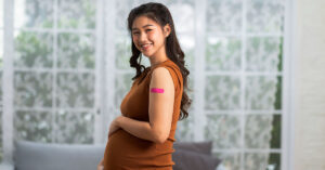 A pregnant woman smiles after receiving a vaccination, with a band aid on her upper left arm